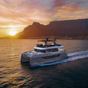 A luxurious catamaran sails on the calm ocean water at sunset with stunning mountain views in the background. This image symbolizes adventure, luxury, relaxation, travel, and nature.